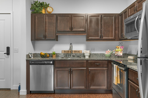 A modern kitchen featuring dark wooden cabinets, a stainless steel dishwasher, and a granite countertop adorned with fruits.