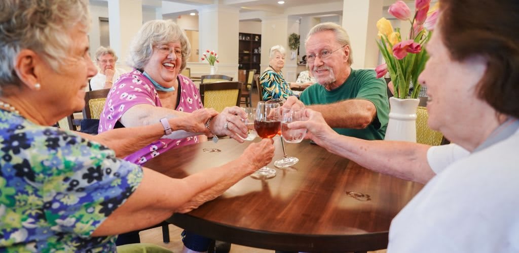 A group of seniors enjoying a celebratory toast with wine around a table.