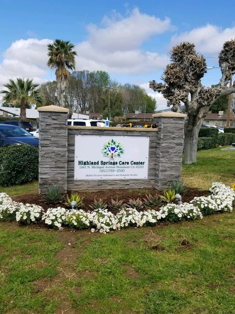 Outdoor sign for a healthcare facility surrounded by flowers and greenery.