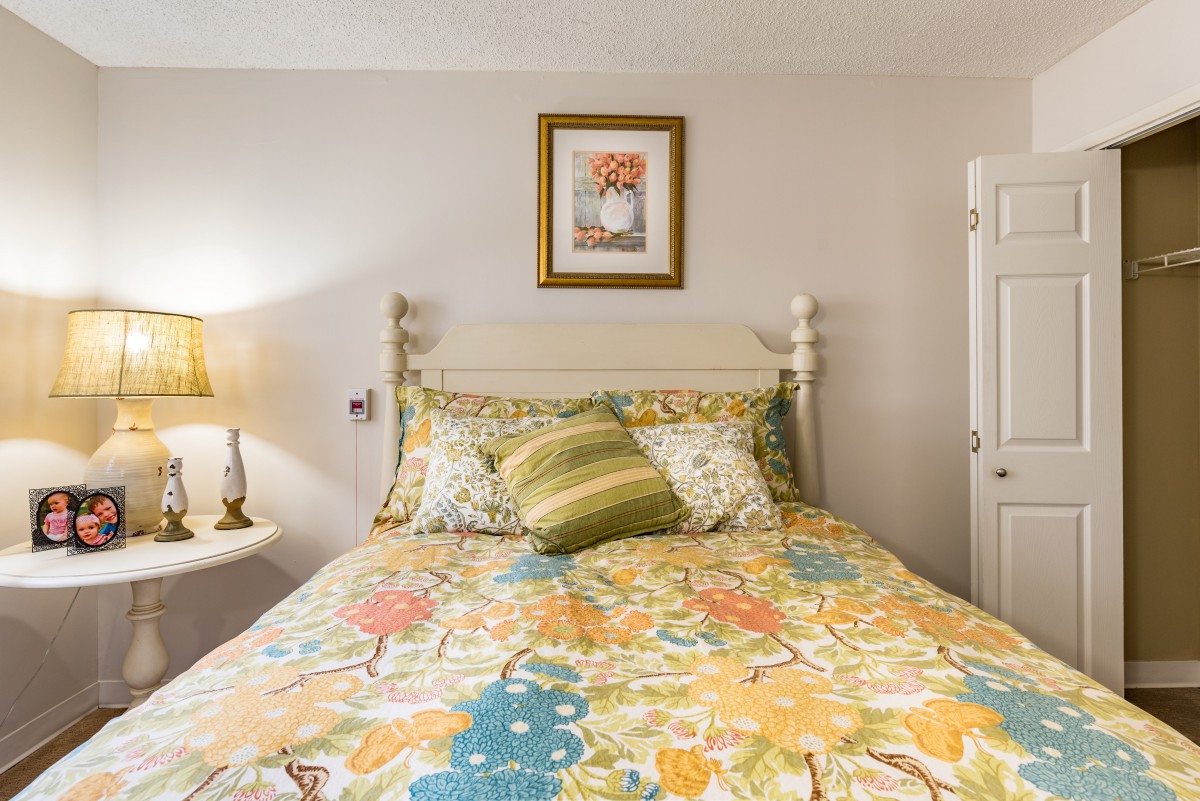 A cozy bedroom featuring a colorful bedspread, decorative pillows, and a lamp on a side table.