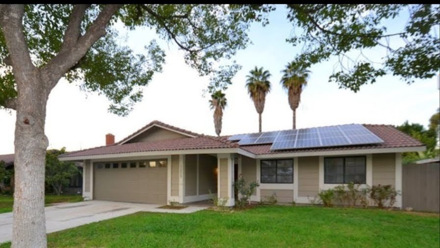 A suburban house with solar panels on the roof and a well-maintained lawn.