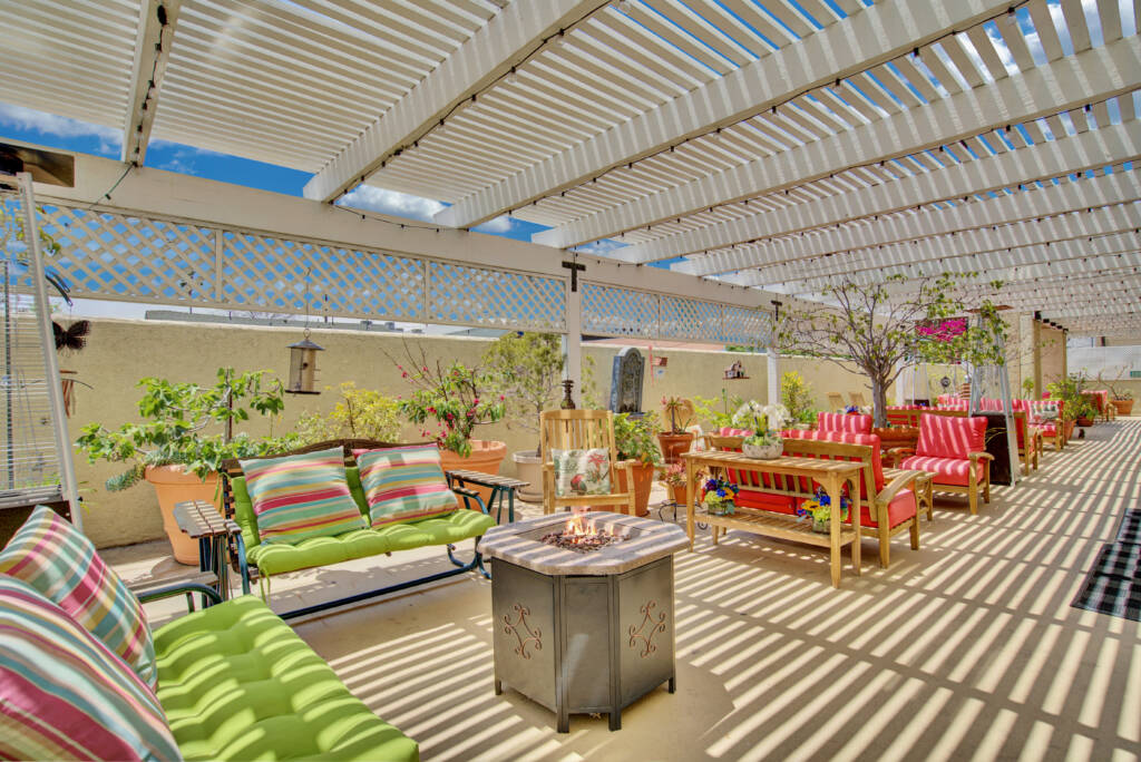 A cozy patio area with a pergola providing shade over vibrant outdoor seating and decor.