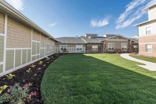 A well-manicured lawn and landscaped garden surround a modern building under a bright blue sky.