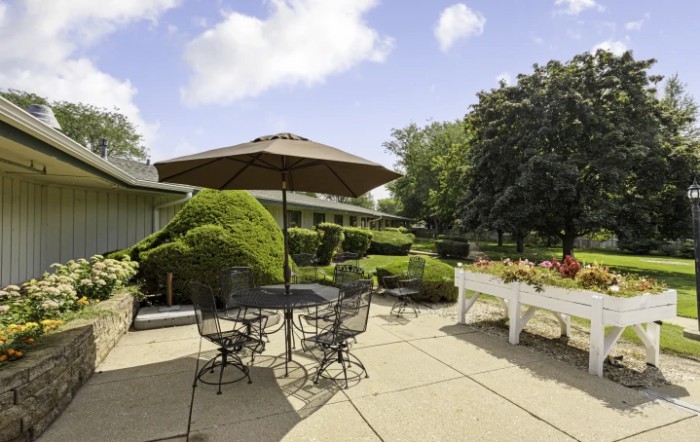 A sunny patio with outdoor seating, including a table and umbrella surrounded by lush greenery.