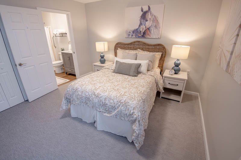 A cozy bedroom with a neatly made bed, flanked by two bedside tables with lamps, and adorned with a piece of horse artwork above the headboard.