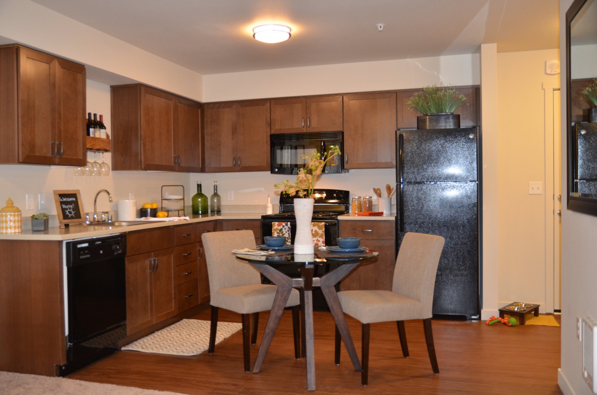 A modern kitchen with a small dining area featuring wooden cabinets, sleek appliances, and contemporary furniture.