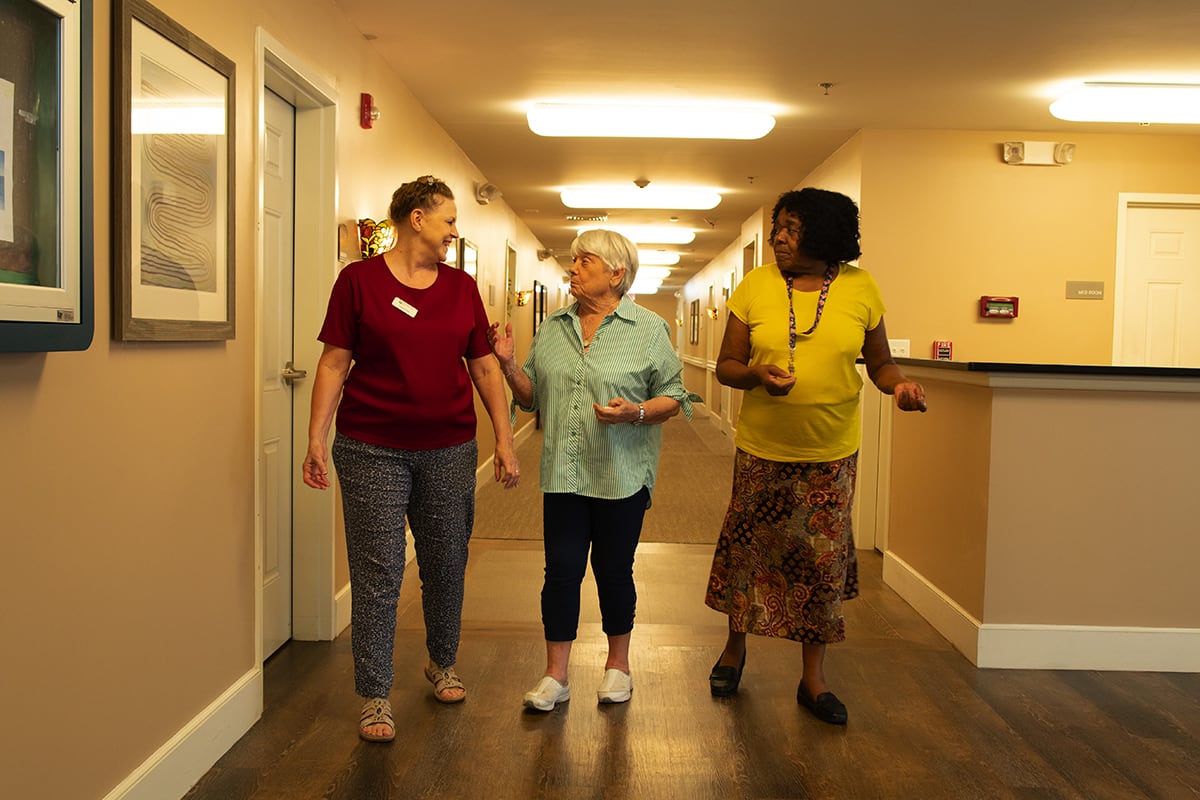 Three women engage in conversation while walking down a hallway.