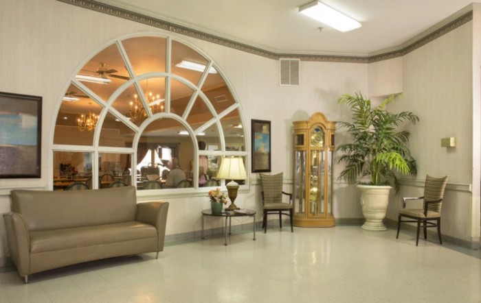 A cozy waiting area with a sofa, chairs, a lamp, and a grandfather clock by large arched windows.