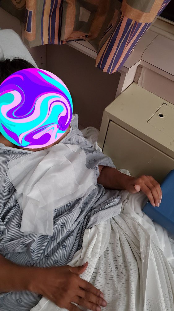 A patient rests in a hospital bed wearing a gown.
