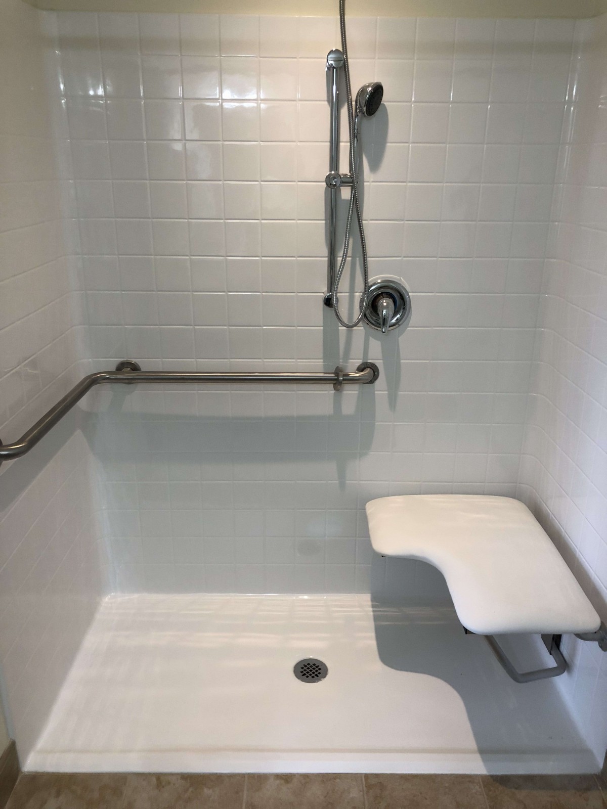 An accessible shower with a grab bar, foldable seat, and handheld showerhead designed for safety.