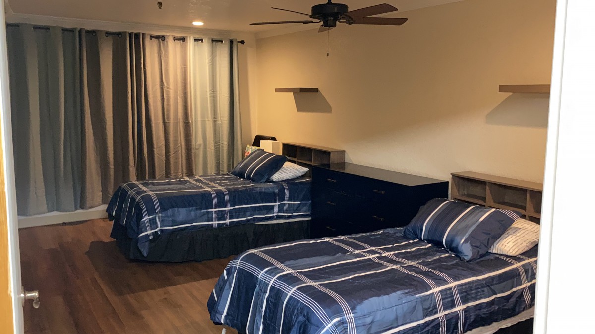 A neatly arranged bedroom featuring two single beds with striped bedding, a ceiling fan, and curtains on the window.
