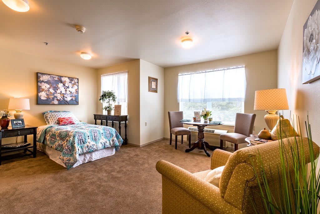 A cozy bedroom with a bed, seating area, and large window.