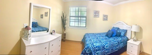 A cozy bedroom with a blue bedspread, white dresser, and natural light from a window.