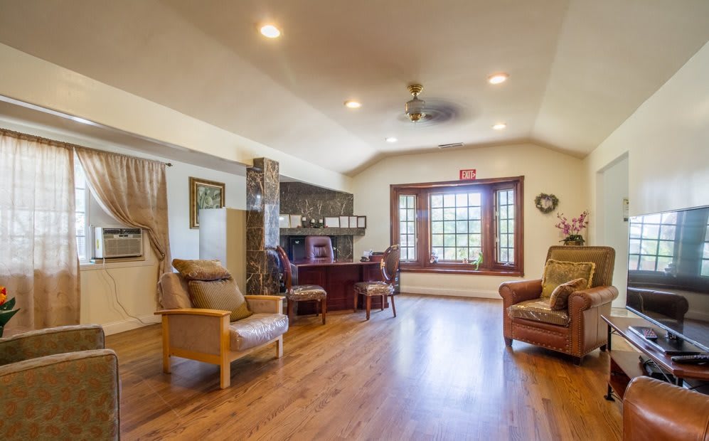 A cozy living room with wooden flooring, featuring comfortable armchairs and a large window.