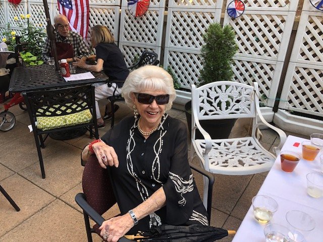 A woman in sunglasses sitting on a patio with an American flag in the background.
