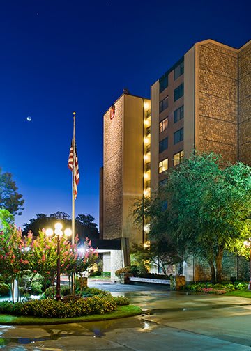 A hotel building illuminated at night with an American flag, surrounded by trees and bright lights.
