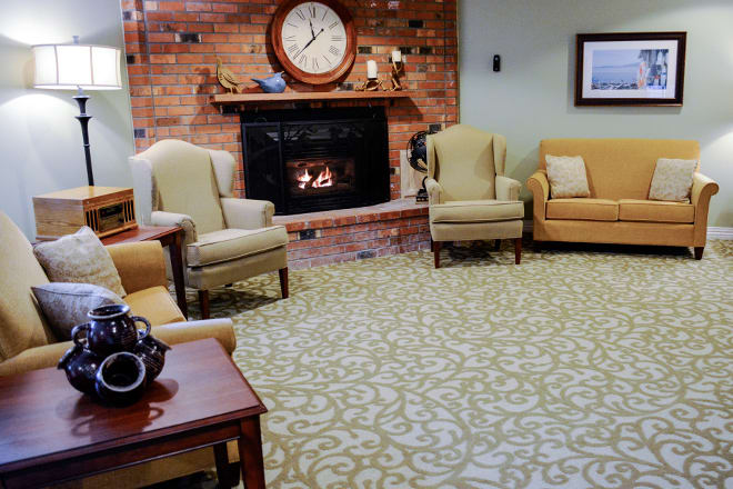 A cozy living room with a brick fireplace, armchairs, and a patterned carpet.