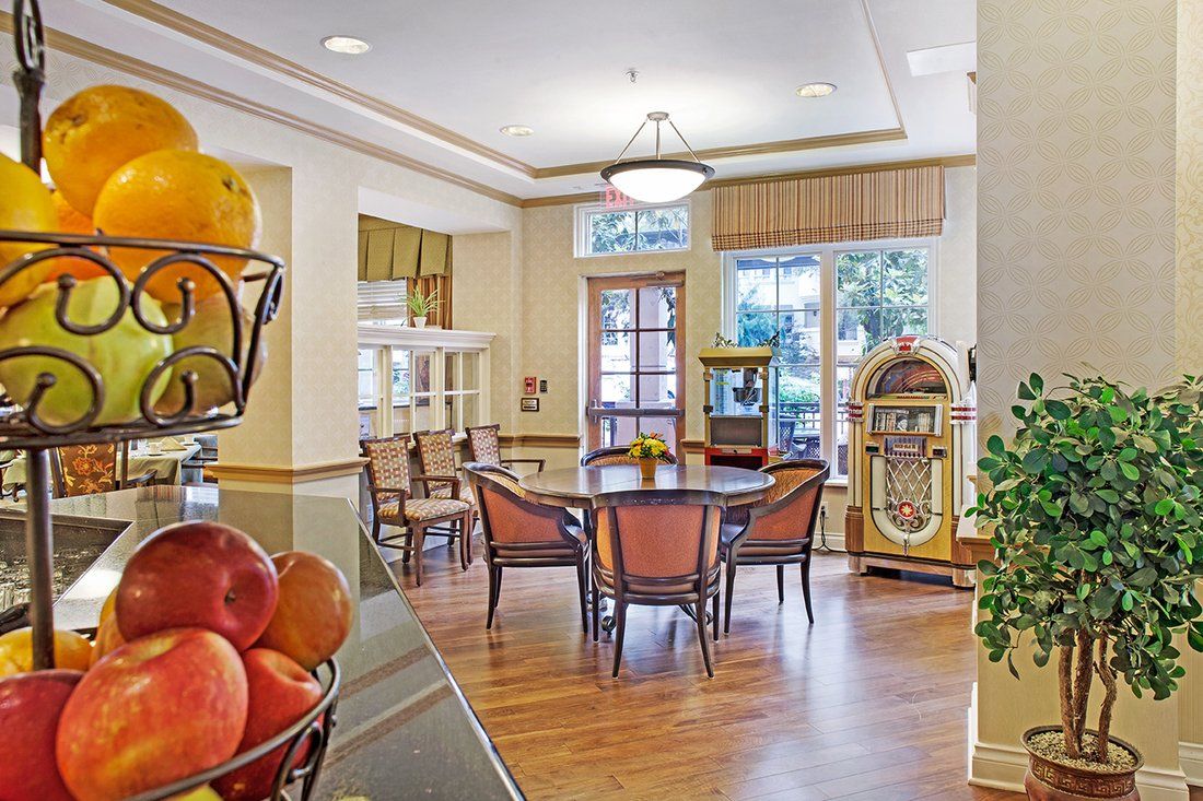 A cozy dining area featuring a round table with chairs, a vintage jukebox, and large windows providing ample natural light.