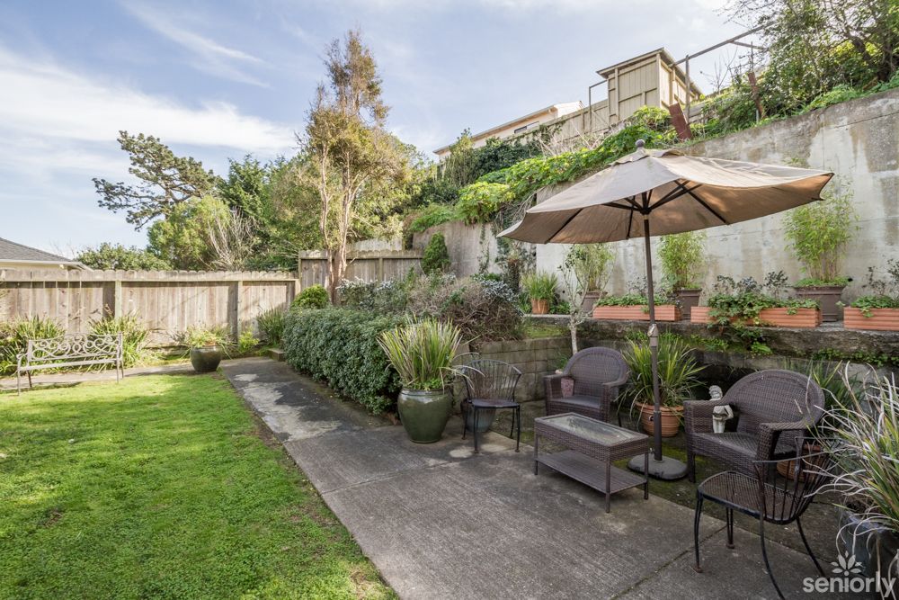 A beautifully landscaped backyard with a cozy patio area, featuring outdoor seating and an umbrella.