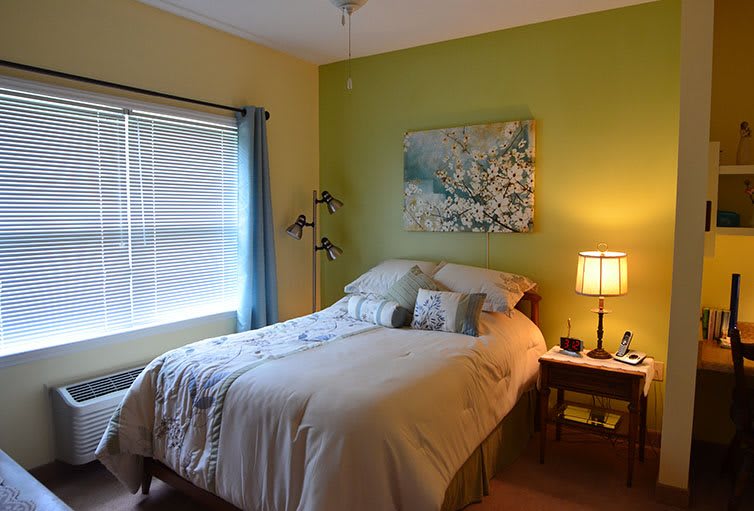 A cozy bedroom with a neatly made bed, soft lighting from a lamp, and wall art above the headboard.