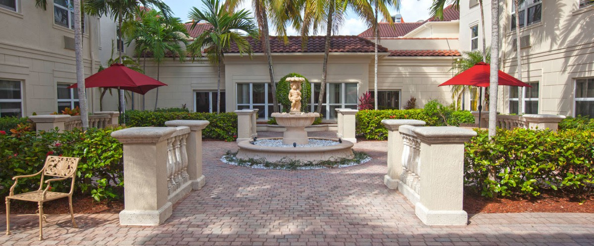 A scenic courtyard featuring a central fountain surrounded by palm trees and elegant landscaping.