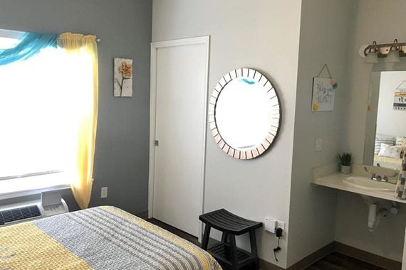 A cozy bedroom with a mirror, bed, and natural light from the window.