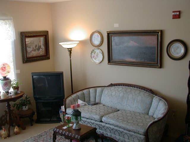 A cozy living room with a vintage sofa, floor lamp, and framed artwork on the walls.