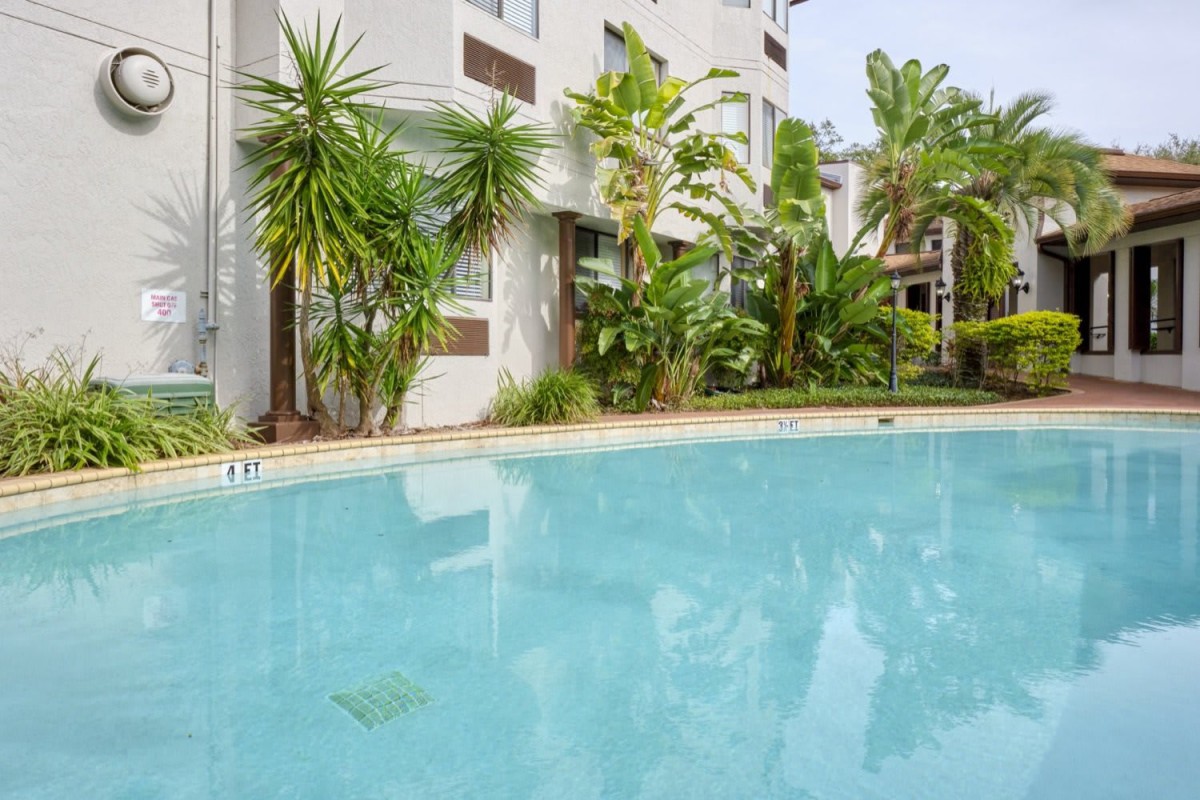 A serene outdoor swimming pool surrounded by palm trees and a modern apartment building.