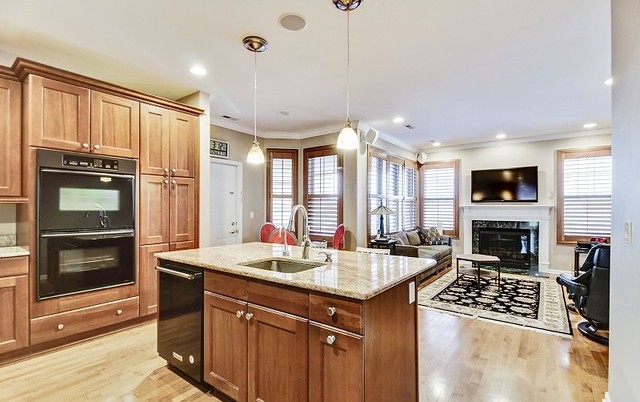 A modern open-concept kitchen and living area featuring an island with wood cabinets, pendant lights, and a cozy fireplace.