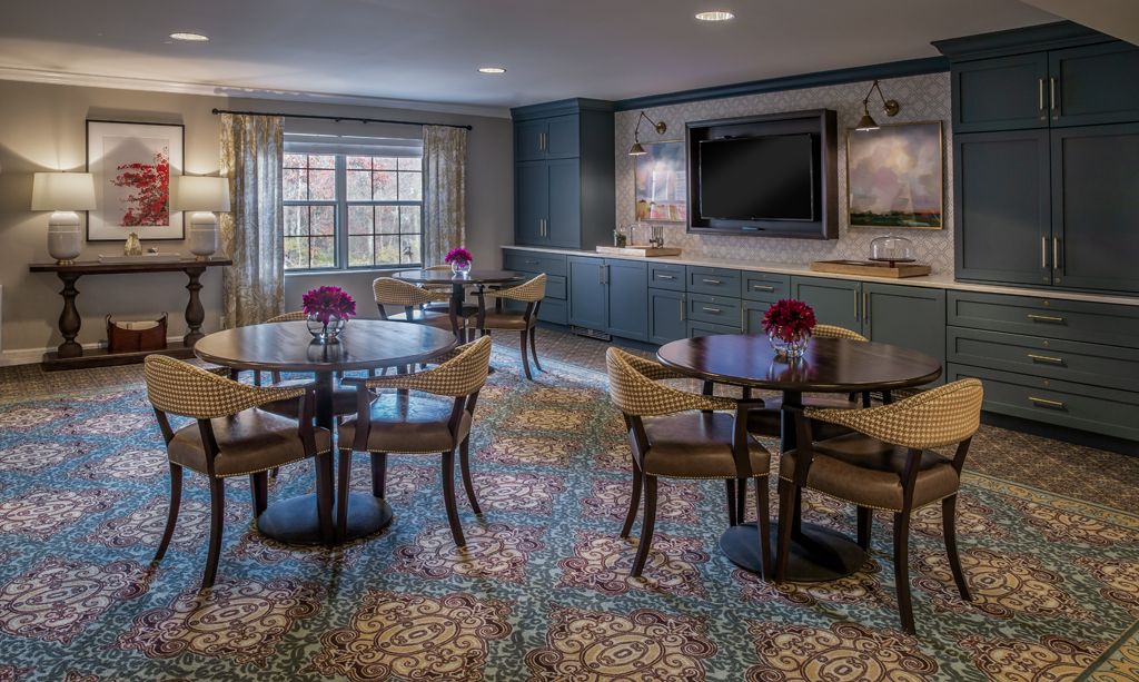 A cozy meeting room with round tables, chairs, and decorative flowers placed beneath a large television.