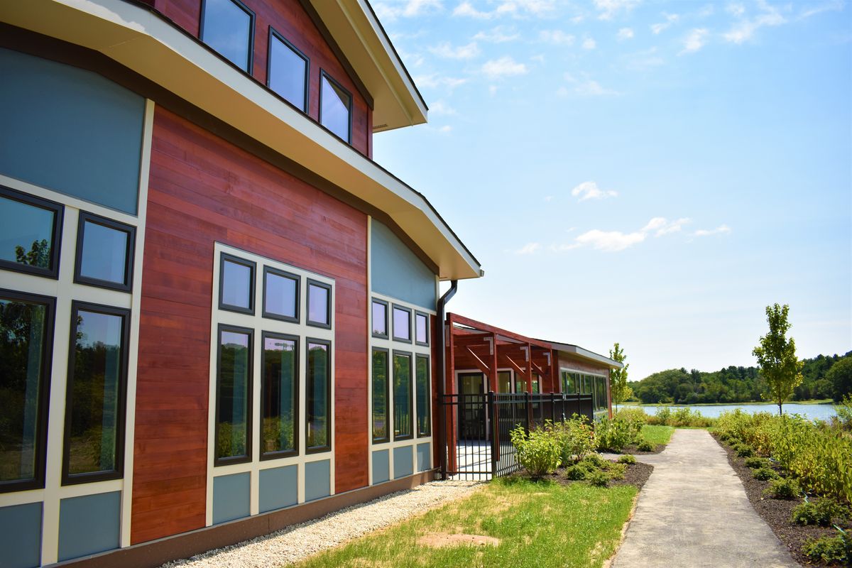 A modern building with large windows and wood paneling, set against a natural outdoor backdrop under a clear sky.