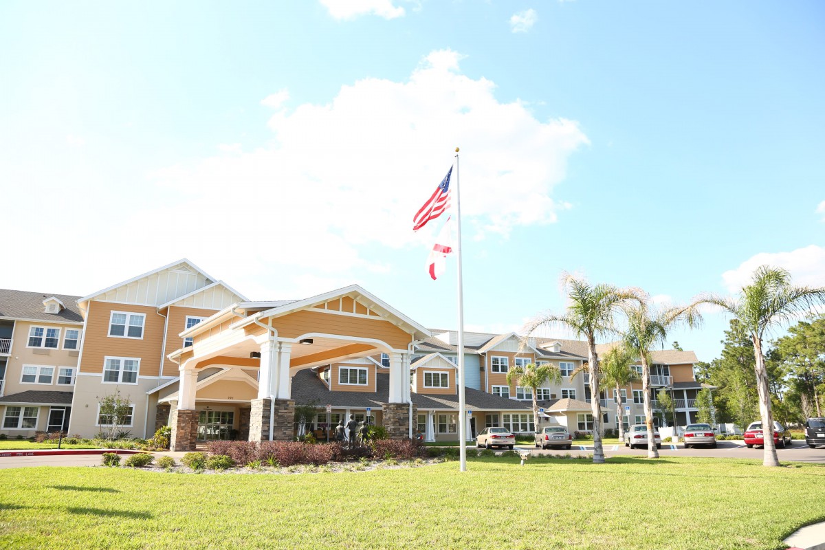 A large building with a flagpole and palm trees on a sunny day.