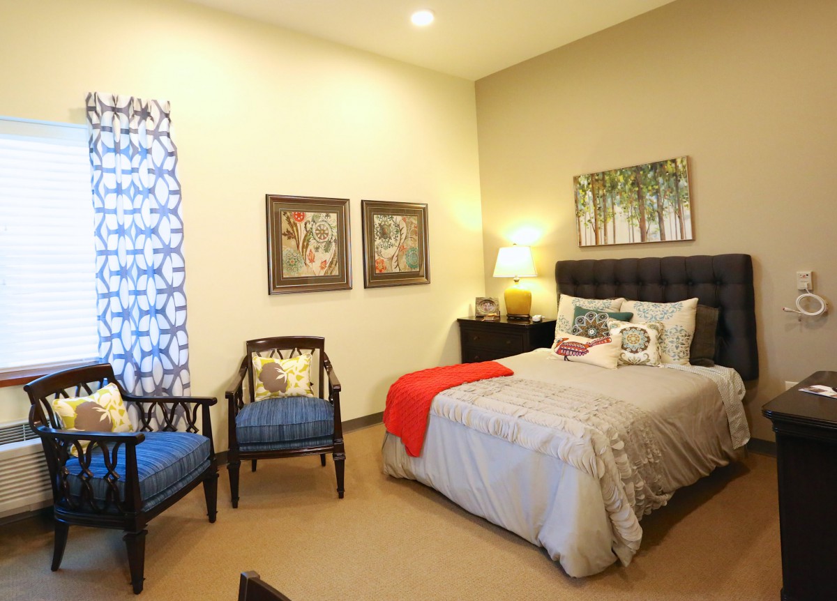 A cozy bedroom with a neatly made bed, two chairs, and stylish decor.