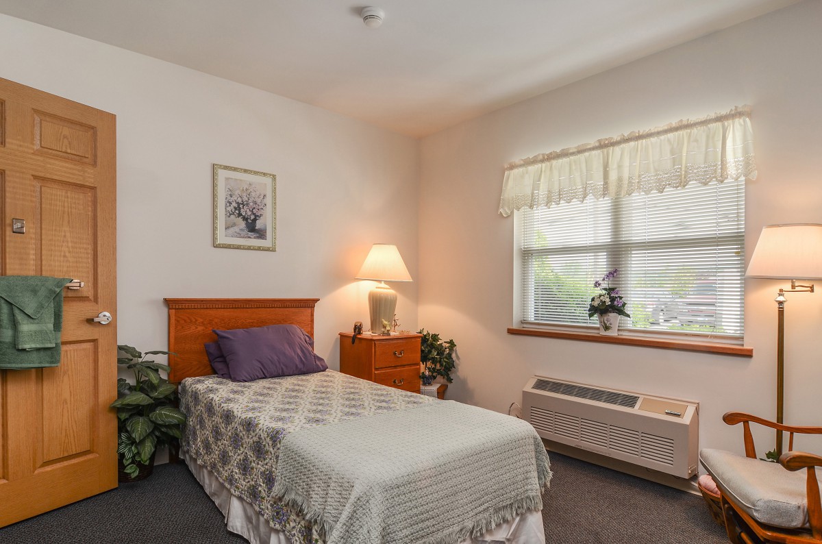 A simple and cozy bedroom with a single bed, dresser, and window.