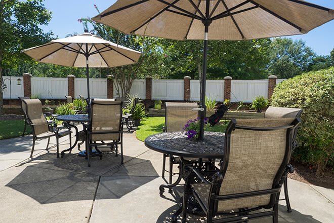 A sunny outdoor patio with tables, chairs, and umbrellas in a garden setting.