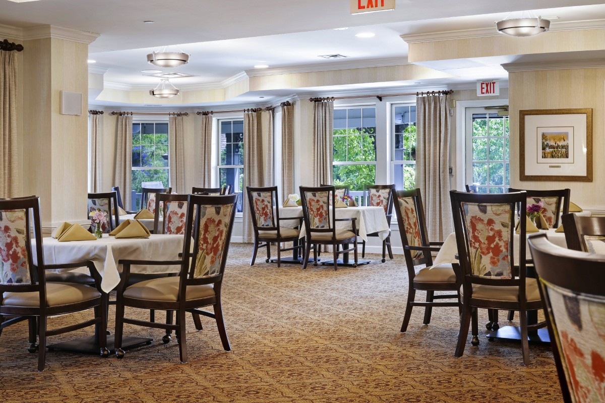 A well-lit dining area with neatly arranged tables and floral upholstered chairs.