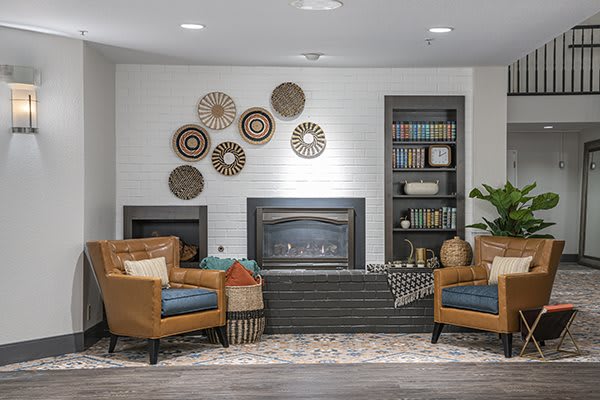 A cozy living room featuring a fireplace, two armchairs, bookshelves, and decorative wall plates.