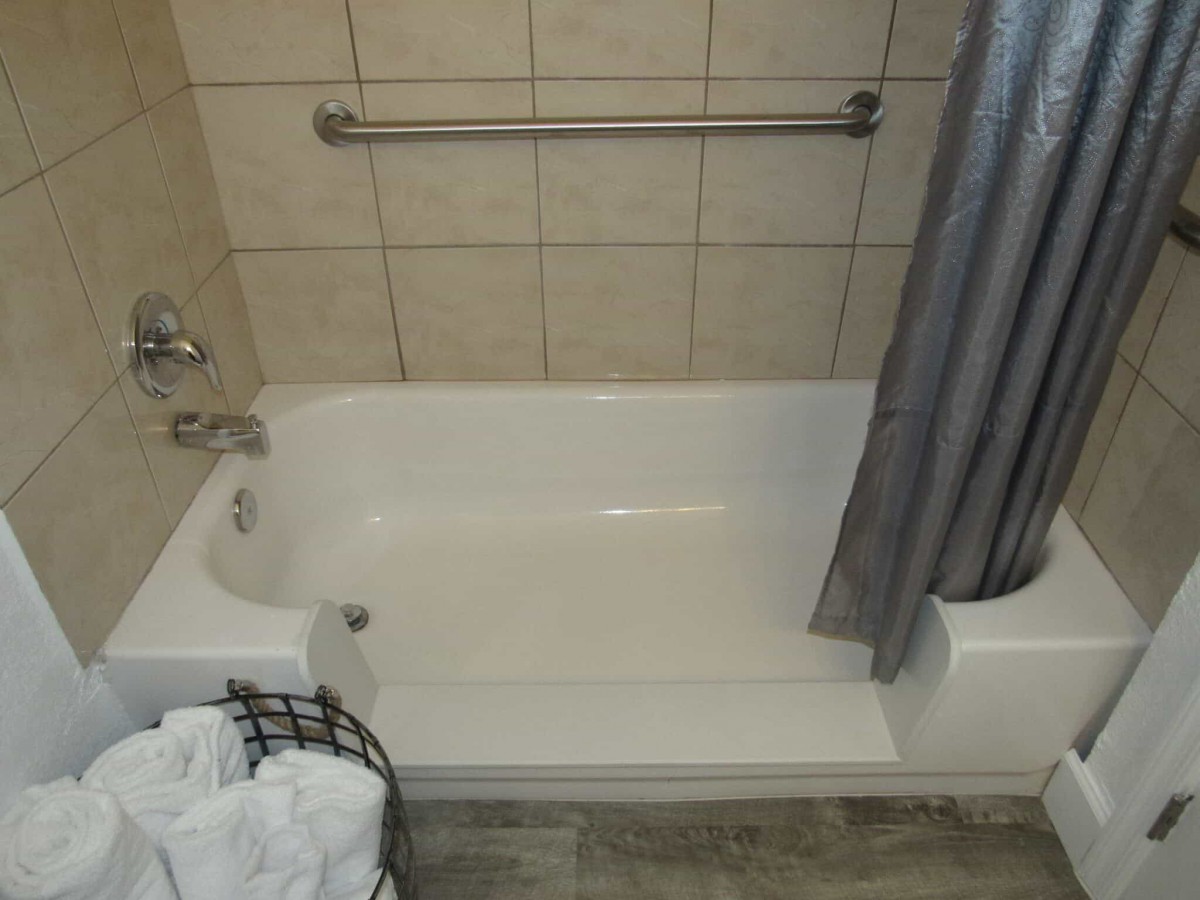 A clean bathtub with a shower curtain and towel basket in a tiled bathroom.
