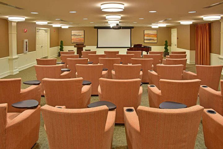 An empty conference room with rows of cushioned chairs facing a projector screen.