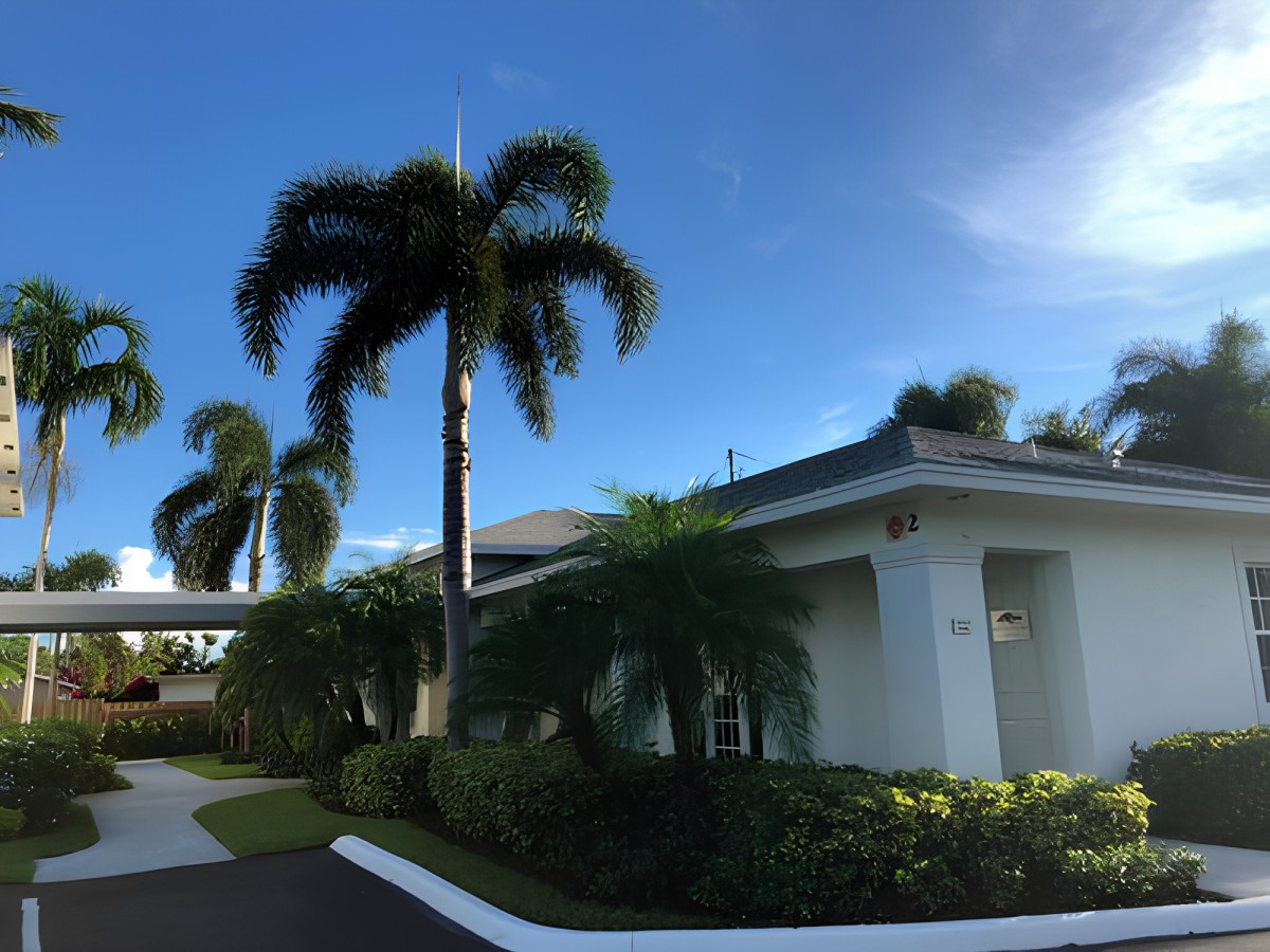 A residential house surrounded by palm trees and lush landscaping under a clear blue sky.