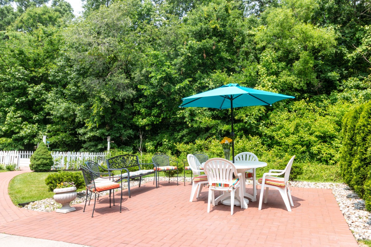A sunny patio area with outdoor seating and a blue umbrella, surrounded by lush greenery.