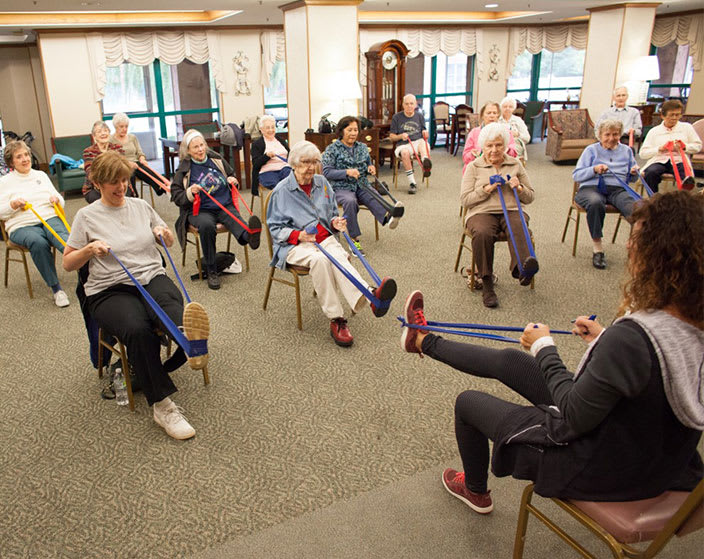 A group of elderly individuals participating in a fitness class using resistance bands at a senior center.