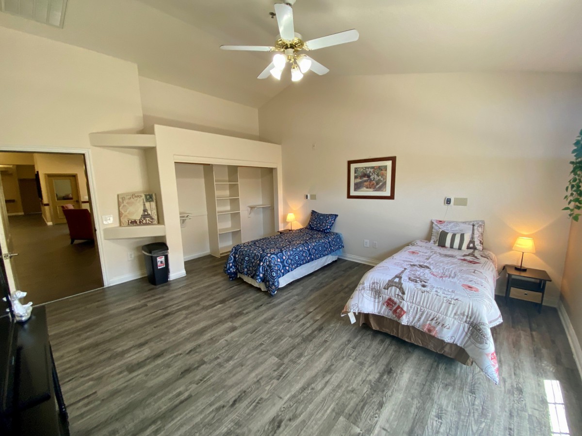 A spacious bedroom with two twin beds, wooden flooring, and a ceiling fan.