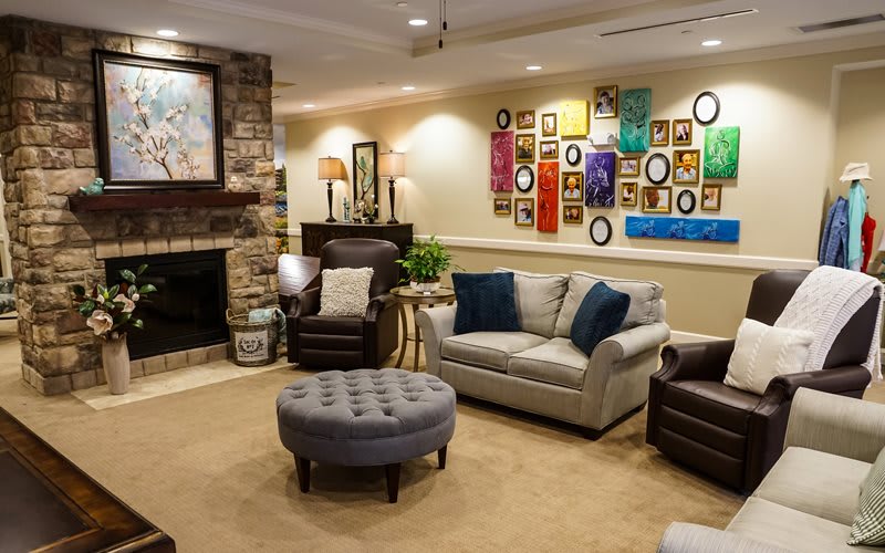 A cozy living room featuring a sofa and armchairs, complemented by an ottoman, fireplace, wall art, and decorative accents.