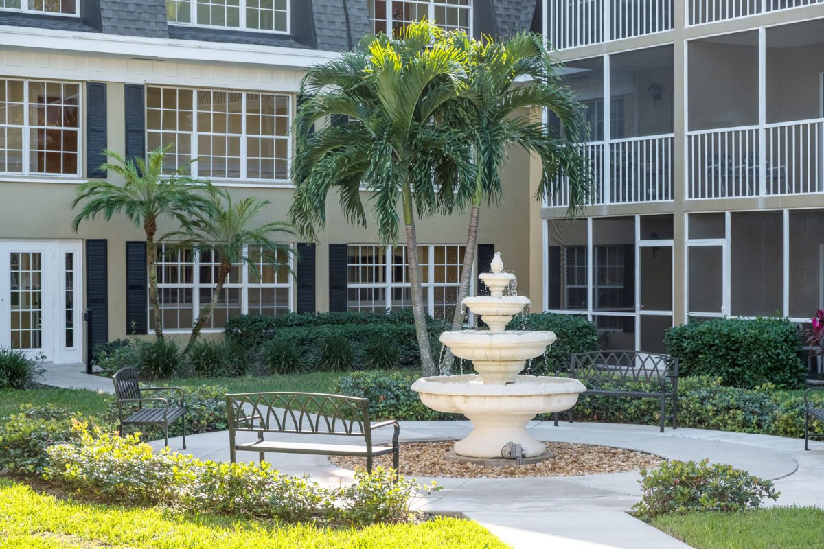 A serene courtyard with a central fountain surrounded by lush greenery and palm trees.