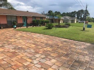 A suburban house with a spacious driveway made of pavers and a well-maintained lawn.