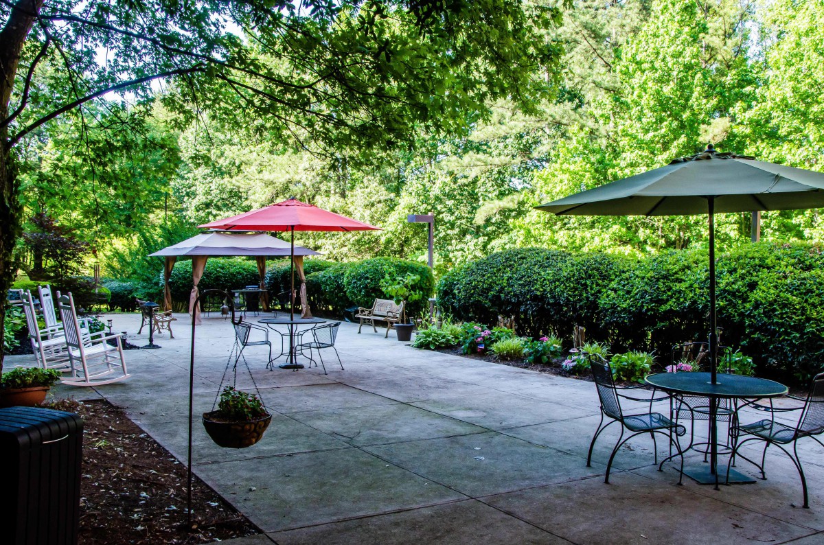 A serene outdoor patio with tables, chairs, and umbrellas surrounded by lush greenery.