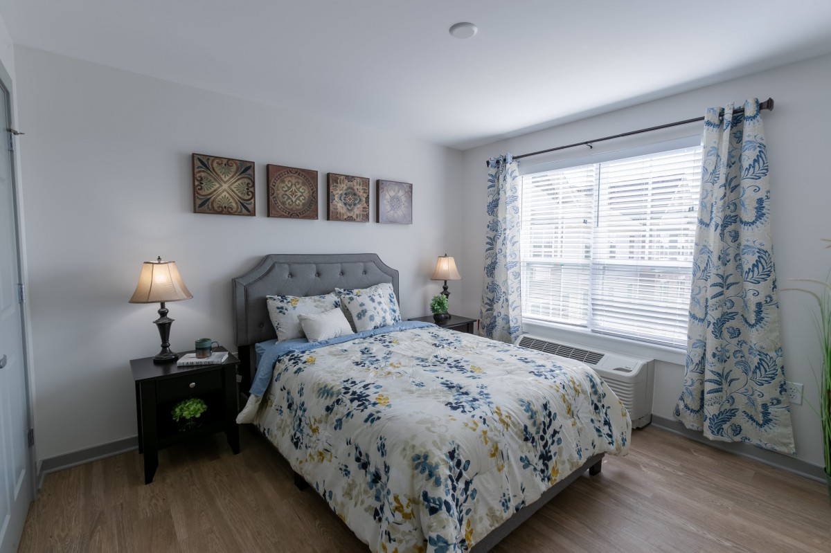 A well-decorated bedroom with floral bedding and ample natural light from a large window.
