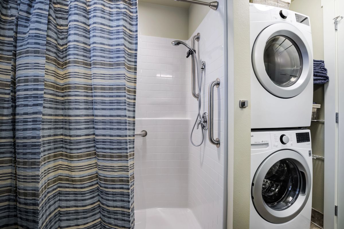A compact bathroom with a shower and an adjacent stacked washer and dryer set.