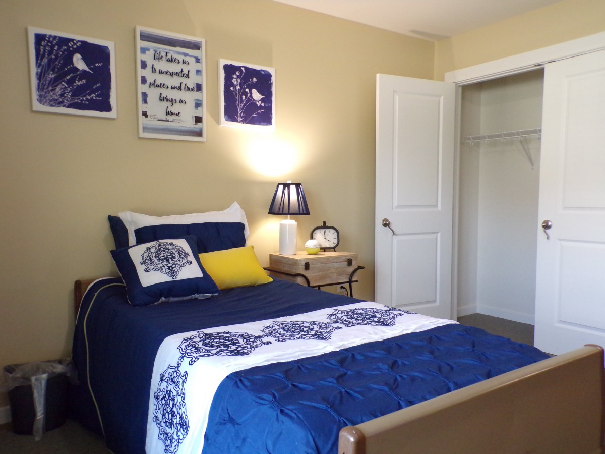 A cozy bedroom with blue-themed decor, featuring a single bed, nightstand, and open closet.
